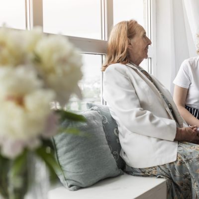smiling-woman-holding-book-sitting-with-her-granny-window-sill